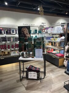 Display of hair care products and holiday gift sets in a well-lit retail store, with shelves stocked with bottles and folded clothing on a lower table. - The Image Salon & Day Spa, CA