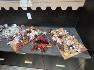 Three trays on a countertop display assorted holiday cookies, berries, chocolates, and festive decorations with a black hexagonal tile backsplash. - The Image Salon & Day Spa, CA