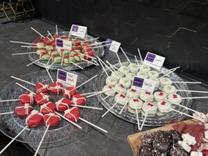 Three trays of decorated cake pops on sticks labeled chocolate, red velvet, lemon, and vanilla, displayed on a counter with a variety of designs and colors. - The Image Salon & Day Spa, CA