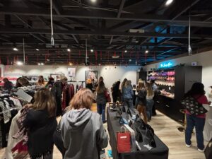 Shoppers browse clothing racks and displays at a well-lit boutique, with several people gathered near a counter and accessories displayed on tables. - The Image Salon & Day Spa, CA